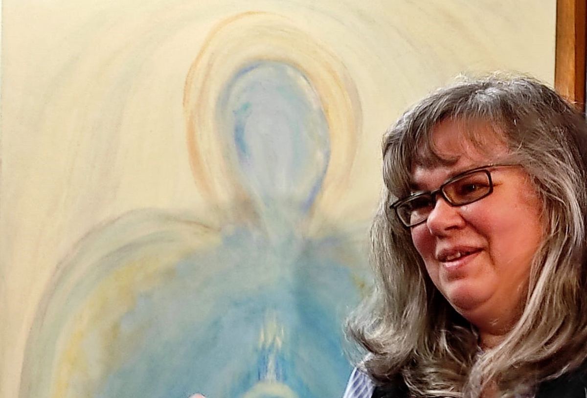 Andrea Marohn erzählt lächelnd, hinter ihr ein großes Bild mit einer hellen Lichtgestalt