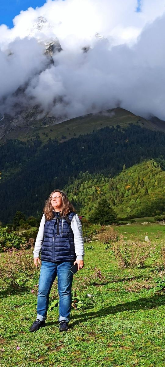 Andrea Marohn steht mit geschlossenen Augen in der Sonne vor einem Berg in den Wolken