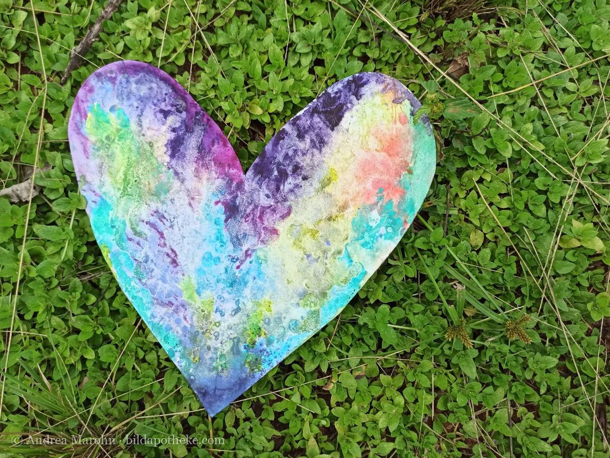 Aquarell: ein bunt marmoriertes Herz, auf einer Wiese fotografiert