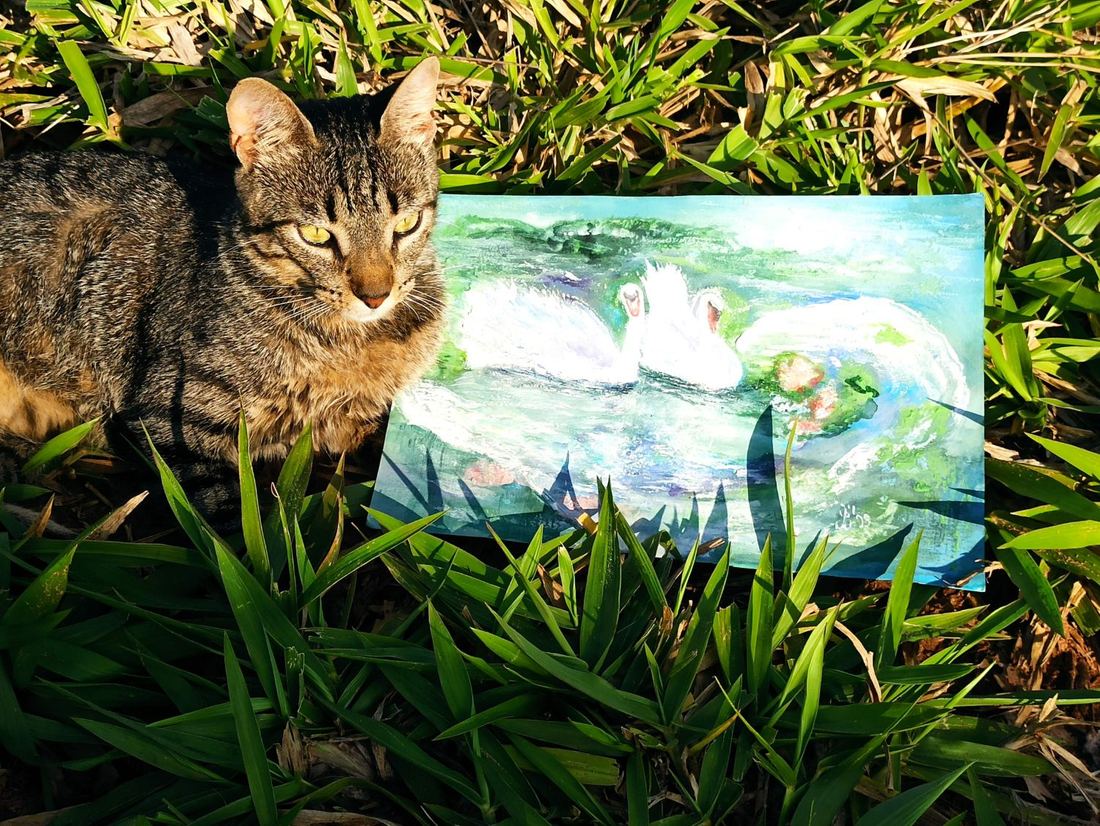 Eine Katze sitzt stolz neben dem Aquarell mit dem Schwanenpaar