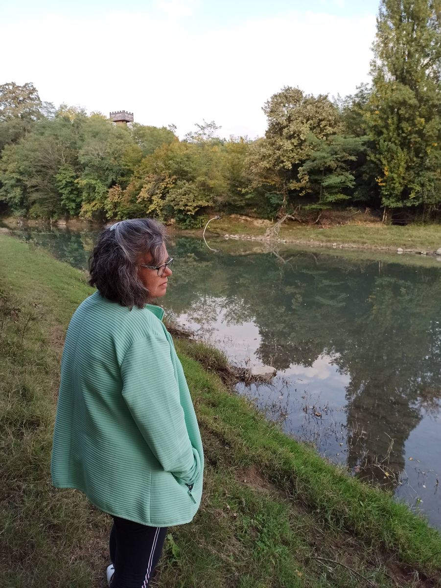 Andrea Marohn in mintgrüner Jacke blickt still auf einen Fluss in Georgien
