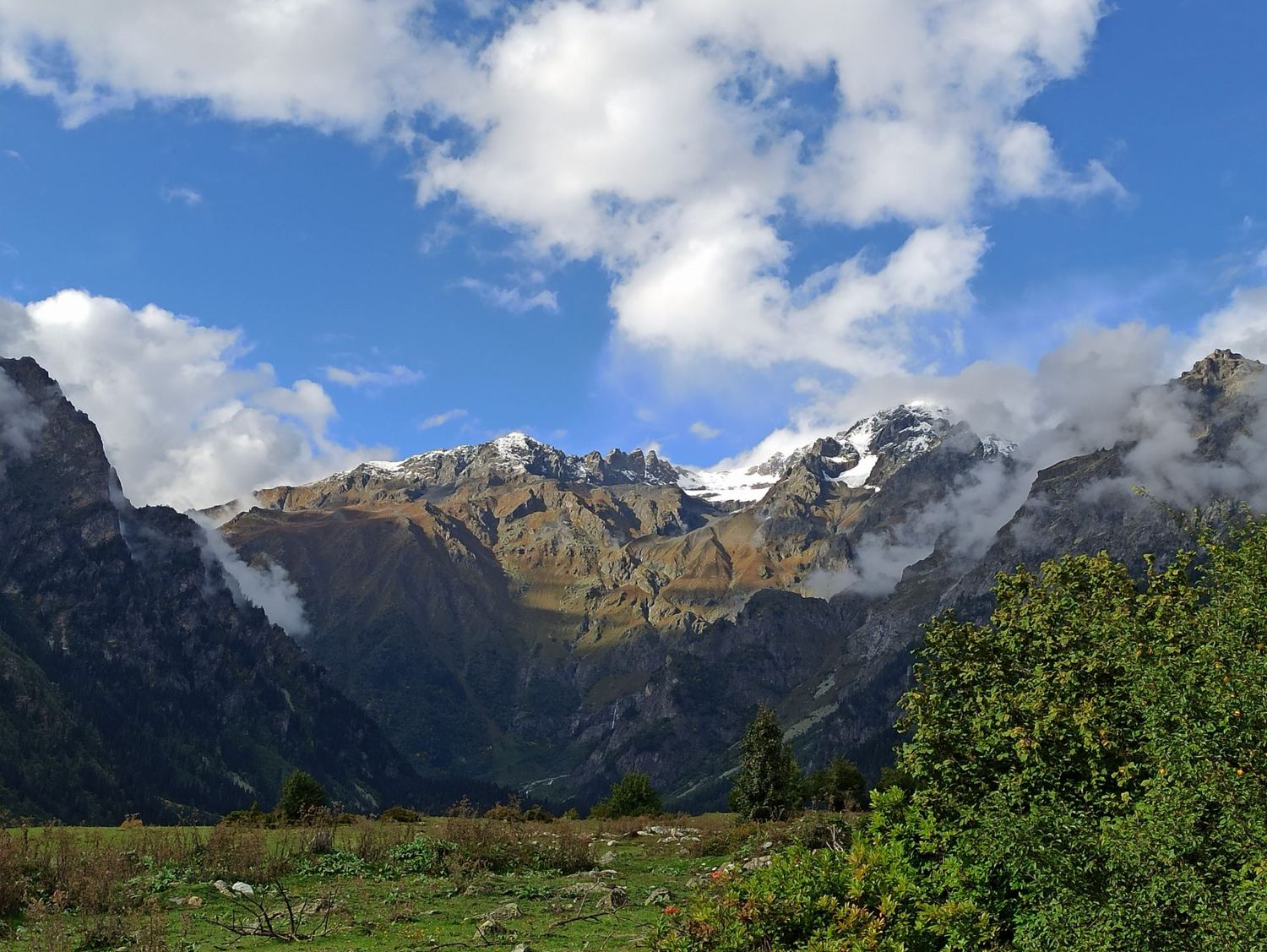Gipfel des Kaukasus mit Wolken über einer grünen Wiese